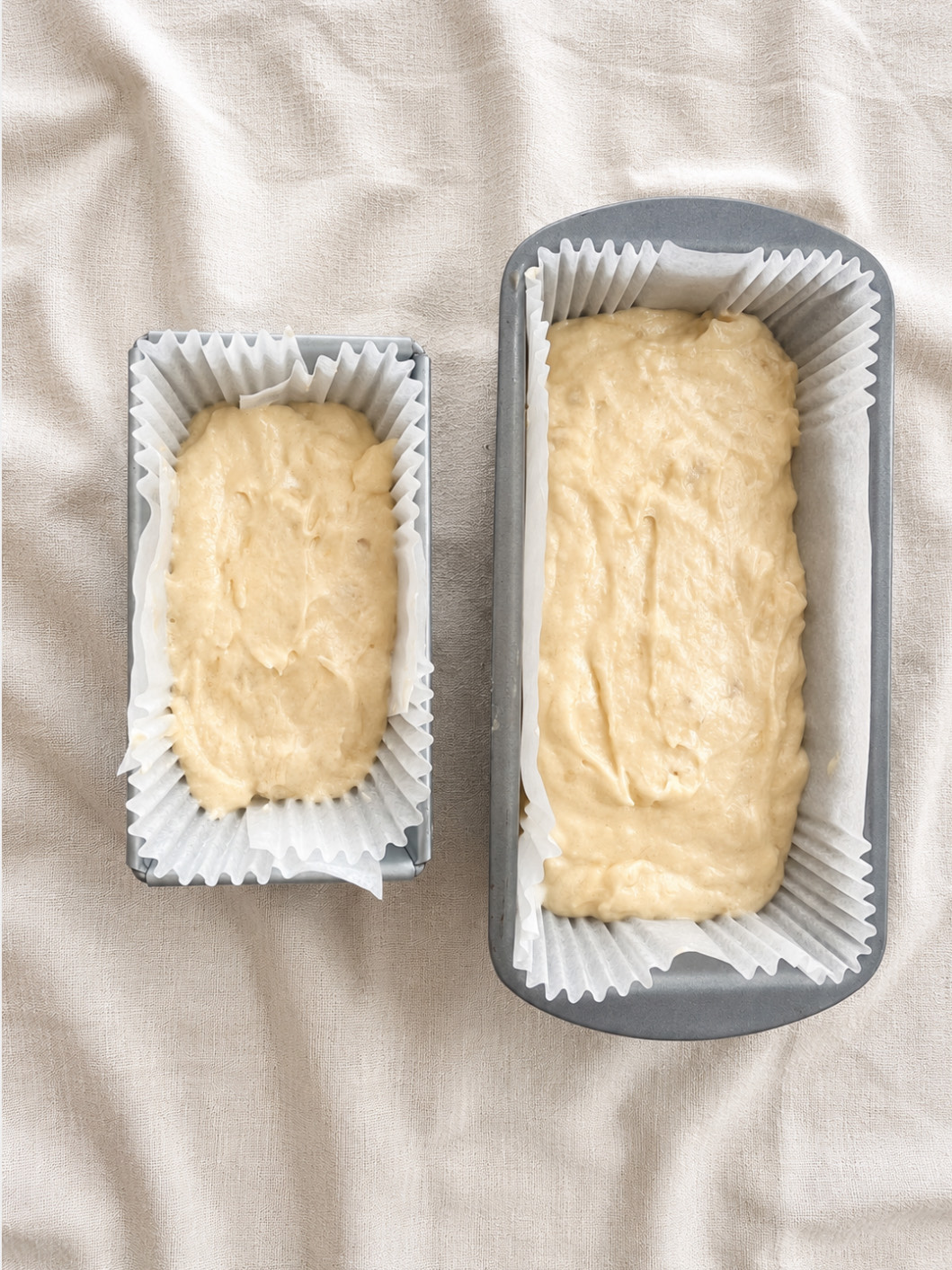 Banana bread batter levelled in two lined loaf tins — one small, one standard — ready for the oven.